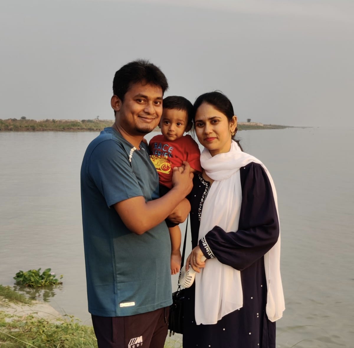 Mahtab, Arham and Anny standing together by a wide river at dusk
